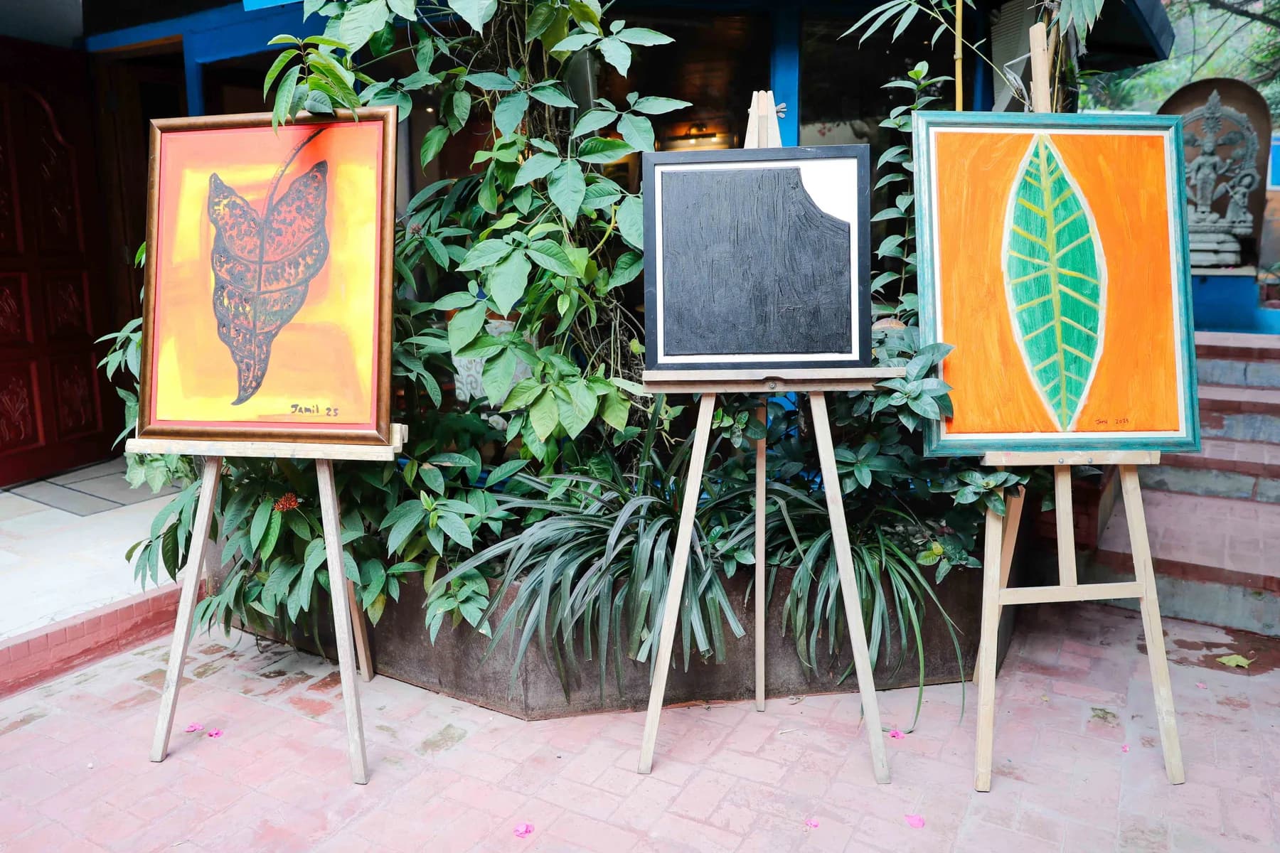 Paintings shown on easels among the planting in the gallery courtyard